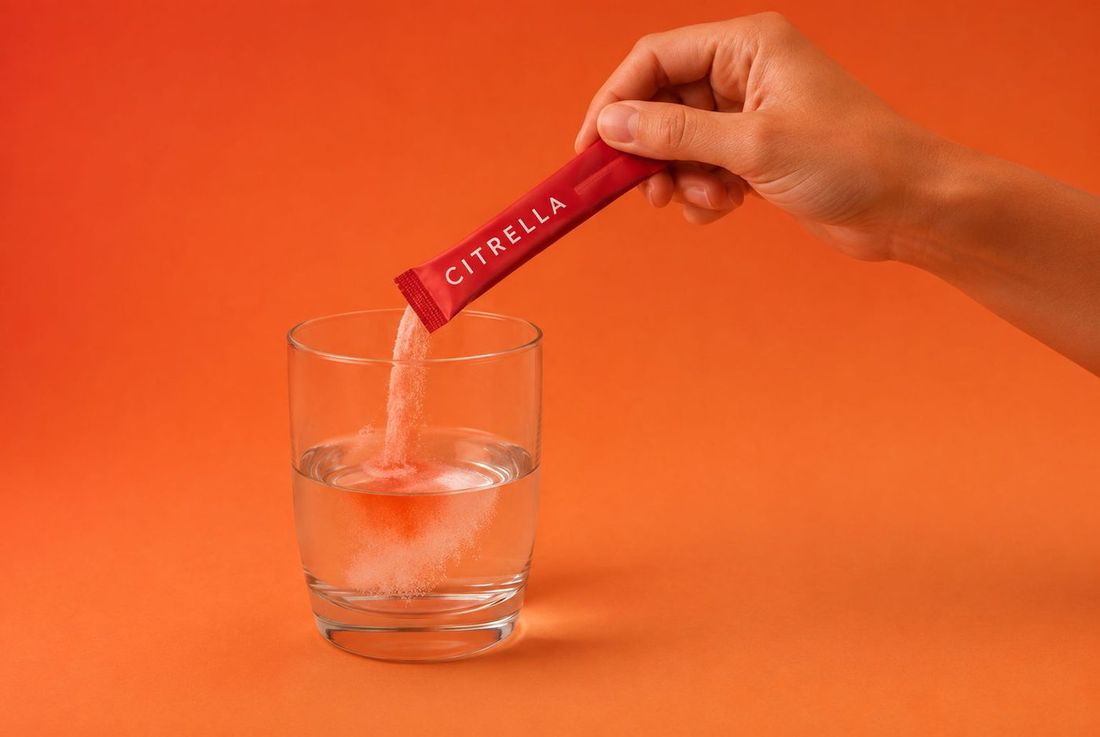 Main versant la poudre d’un slim stick Citrella dans un verre d’eau